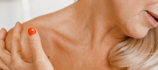 How stress effects your skin. Woman looking down showing the skin on her collarbone, her hand is resting on her shoulder and she has bright orange nail polish on.